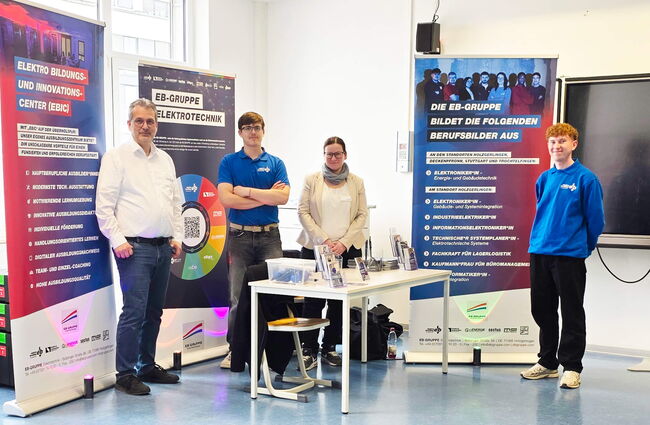 Vier Personen stehen an einem Tisch im Elektro Bildungs- und Innovationscenter, um Informationen über Elektrotechnik auszutauschen.