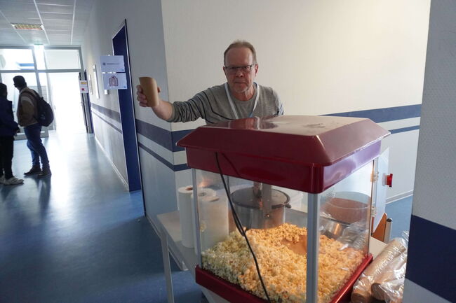 Ein Mann steht in einem Flur und hält einen Pappbecher neben einer Popcornmaschine.