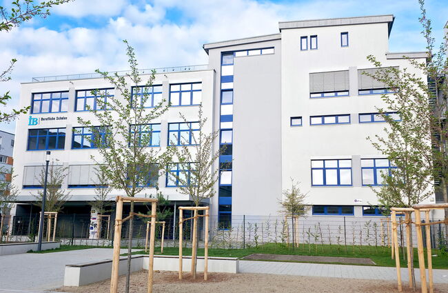 Ein modernes Schulgebäude mit großen Fenstern und einem gepflegten Außenbereich, umgeben von jungen Bäumen.