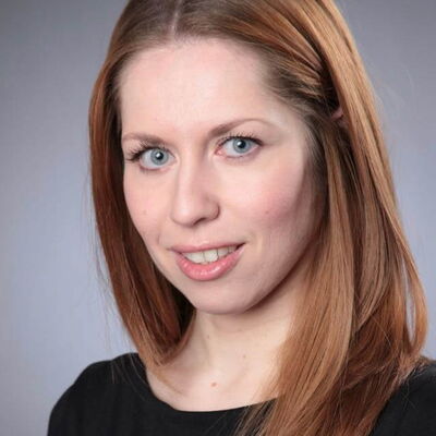 Eine Frau mit langen, roten Haaren und blauen Augen lächelt freundlich in die Kamera.