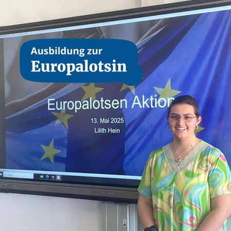 Eine Frau steht lächelnd vor einer Präsentation mit dem Titel "Europalotsen Aktion" auf einem Bildschirm.