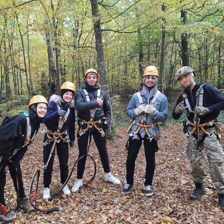 Eine Gruppe von fünf Personen steht im Herbstwald in Kletterausrüstung und lächelt in die Kamera.