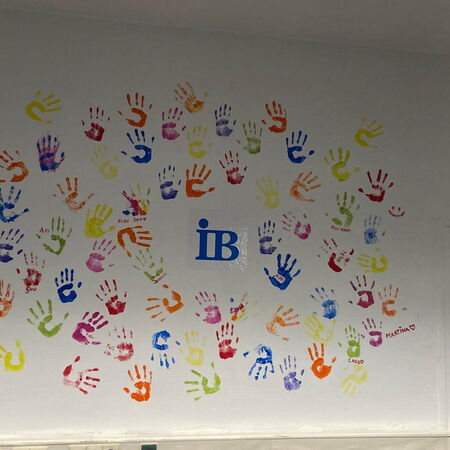 Bunte Handabdrücke in verschiedenen Farben umgeben das blaue "iB"-Logo auf einer weißen Wand.