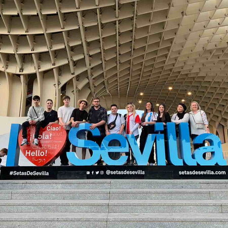 Eine Gruppe junger Menschen posiert fröhlich vor dem "I Love Sevilla"-Schriftzug unter der beeindruckenden Holzkonstruktion.