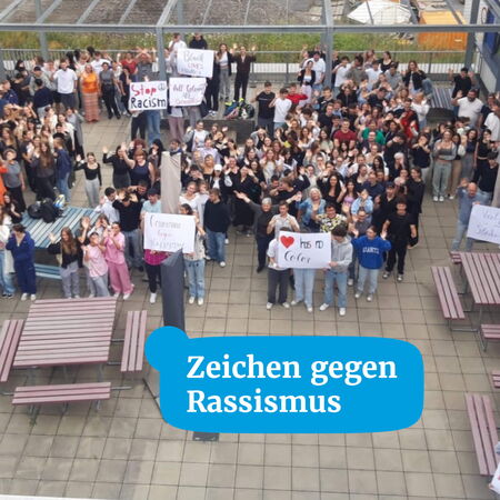 Eine große Gruppe von Menschen versammelt sich mit Schildern, um ein Zeichen gegen Rassismus zu setzen.
