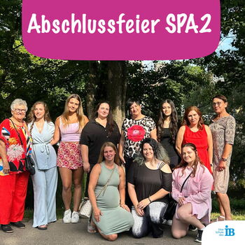 Eine Gruppe von Frauen posiert bei einer Abschlussfeier im Freien vor Bäumen mit einem Schild "Abschlussfeier SPA2".