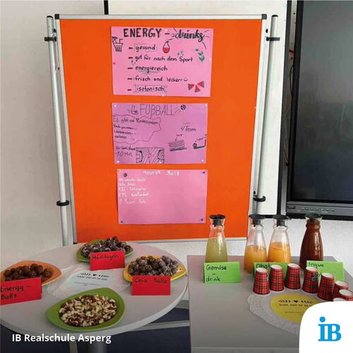 Ein Tisch mit gesunden Snacks und Getränken ist vor einer Infotafel bei einem Schulfest der IB Realschule Asperg aufgebaut.