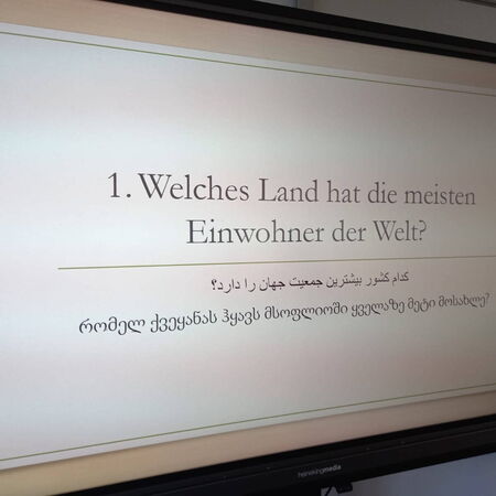 Eine Präsentationsfolie zeigt die Frage: "Welches Land hat die meisten Einwohner der Welt?" in verschiedenen Sprachen.