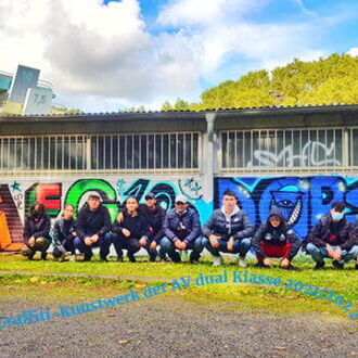 Eine Gruppe posiert vor einer bunten Graffiti-Wand bei einem Workshop im Freien an einem sonnigen Tag.