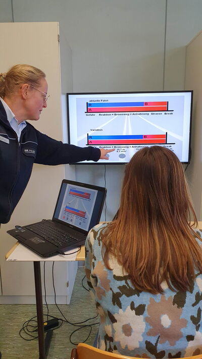 Eine Polizistin erklärt einer Frau an einem Bildschirm mit Diagrammen Verkehrssicherheitskonzepte.