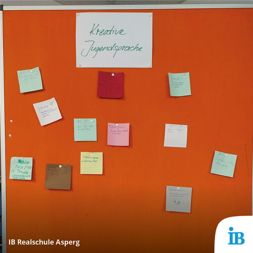 Notizzettel mit kreativer Jugendsprache sind an einer orangefarbenen Pinnwand beim Tag der offenen Tür befestigt.