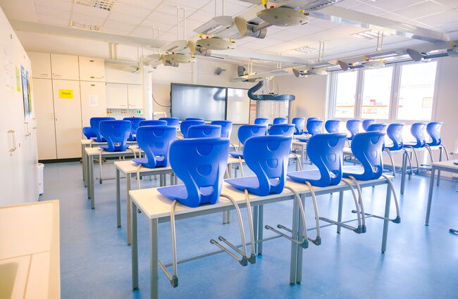 Ein moderner Physikraum und Chemieraum zeigt leere Tische mit blauen Stühlen, bereit für den Unterricht.