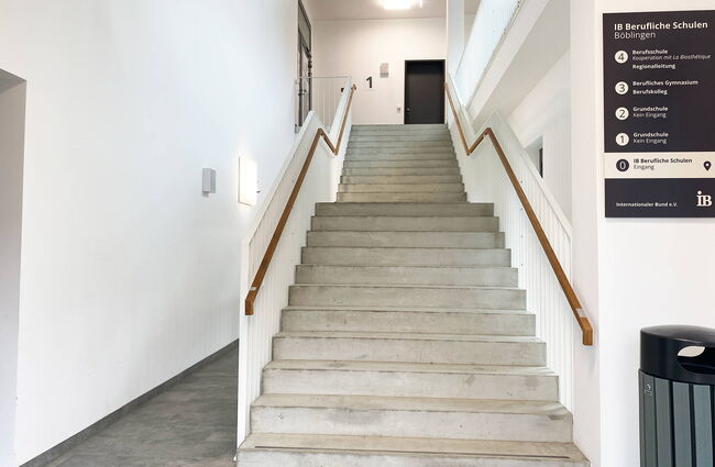 Der helle Eingangsbereich der IB Beruflichen Schulen Böblingen zeigt eine moderne Treppe mit Geländer und Wandbeschilderung.
