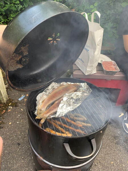 Frische Forellen werden in Alufolie auf einem runden Grill im Freien geräuchert, während Rauch aufsteigt.