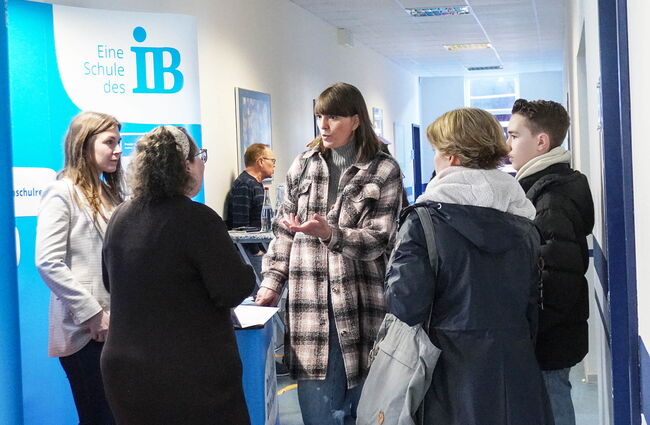 Eine Lehrkraft erklärt interessierten Besuchern die Angebote der Schule des IB in einem Flur.