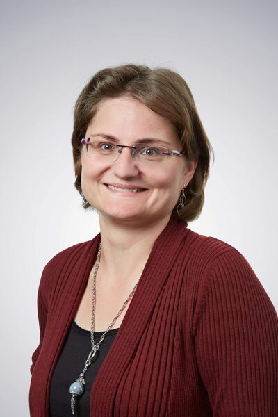 Eine Frau mit Brille lächelt freundlich in die Kamera und trägt ein weinrotes Oberteil und eine lange Halskette.