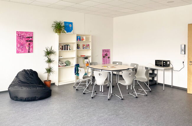 Ein moderner Aufenthaltsraum im Neubau mit einem Tisch, Stühlen und einer gemütlichen Ecke zum Entspannen.
