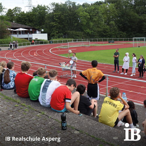 Schüler der IB Realschule Asperg beobachten gespannt eine Sportveranstaltung auf der Laufbahn bei den Bundesjugendspielen.