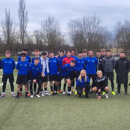 Eine Fußballmannschaft in blauen Trikots posiert gemeinsam auf einem grünen Spielfeld, umgeben von kahlen Bäumen.