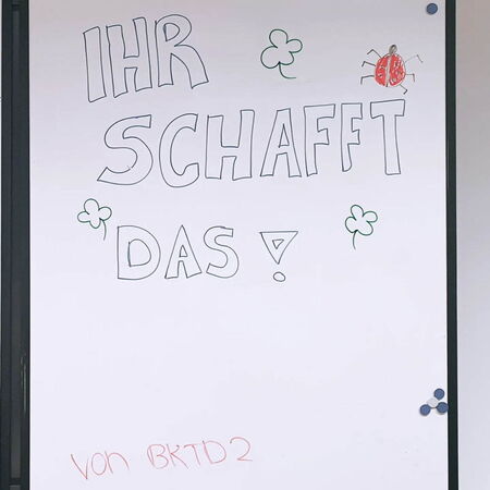 Eine Tafel zeigt die motivierende Botschaft "Ihr schafft das!" mit Klee und einem Marienkäfer verziert.