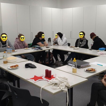 Eine Gruppe von Menschen sitzt um einen Tisch und genießt gemeinsam eine Backrunde in einem hellen Raum.