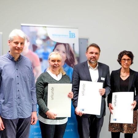 Vier Personen stehen nebeneinander, drei halten Zertifikate in den Händen und lächeln in die Kamera.