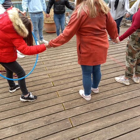 Kinder halten sich an den Händen, während eines Spiels mit einem Hula-Hoop-Reifen auf einem Holzboden.
