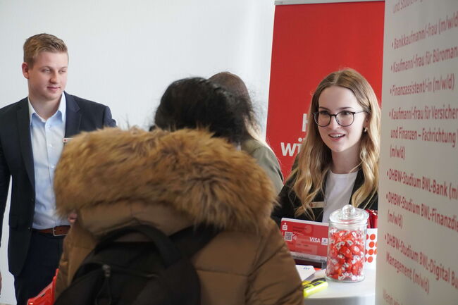 Zwei Personen beraten eine Besucherin an einem Informationsstand über verschiedene berufliche Möglichkeiten.