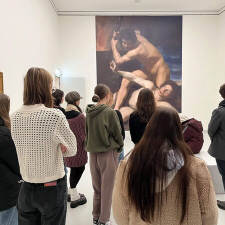 Eine Gruppe von Menschen betrachtet in einem Museum ein großes Gemälde, während eine Führung stattfindet.