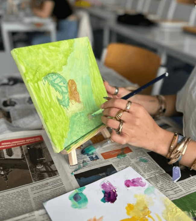 Eine Person malt mit Aquarellfarben auf einer Leinwand während eines kreativen Projekttags.