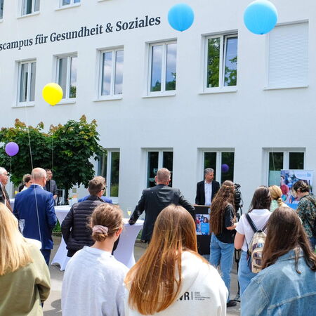 Eine Gruppe von Menschen versammelt sich vor dem Bildungsgebäude, während bunte Luftballons in der Luft schweben.