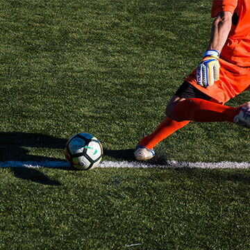 Ein Fußballspieler in orangener Ausrüstung tritt den Ball während eines Turniers auf einem grünen Spielfeld.
