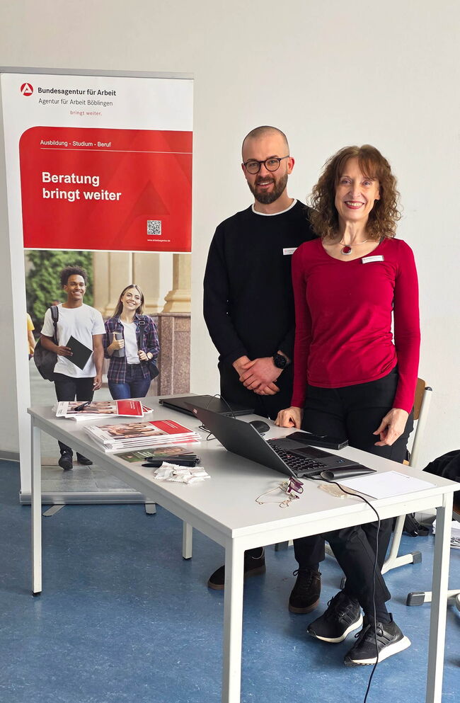 Ein Beraterteam der Bundesagentur für Arbeit steht an einem Tisch mit Informationsmaterialien zur Beratung über Ausbildung und Beruf.