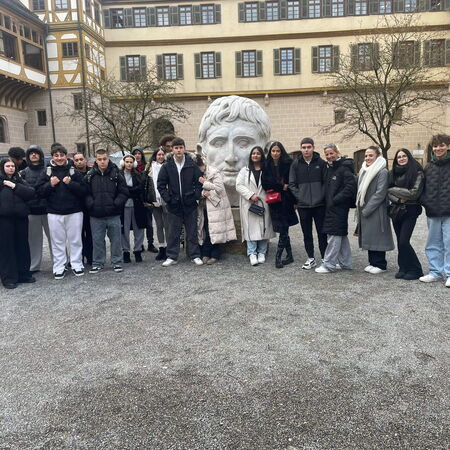 Eine Gruppe junger Menschen posiert vor einem großen Kopf-Skulptur auf einem historischen Innenhof.