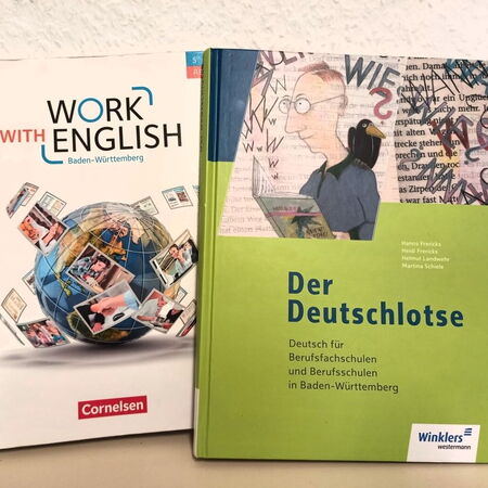Zwei Schulbücher, "Work with English" und "Der Deutschlotse", stehen nebeneinander auf einem Tisch.