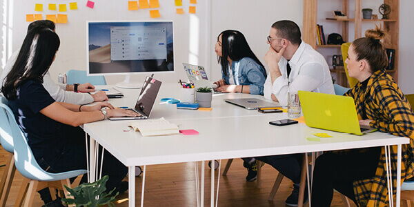 Fünf Personen diskutieren in einem modernen Büro über Schulsozialarbeit, umgeben von Laptops und Notizen.