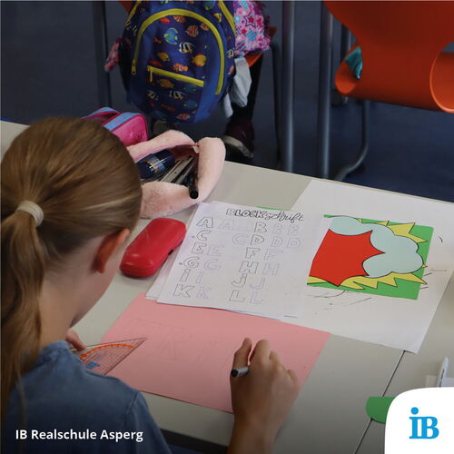 Ein Kind sitzt an einem Tisch und übt Blockschrift auf einem Blatt Papier während des Schulfestes.