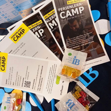 Flyer und Süßigkeiten für ein Ferienlern-Camp liegen auf einem Tisch neben einem Kalender und einem blauen Stift.