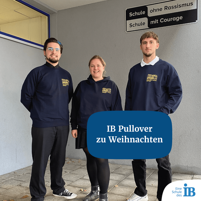 Drei Personen posieren in IB-Pullovern vor einem Schild mit der Aufschrift "Schule ohne Rassismus, Schule mit Courage".