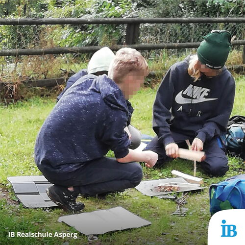 Jugendliche der 8a der Realschule sitzen im Schullandheim auf der Wiese und arbeiten gemeinsam an einem Projekt.