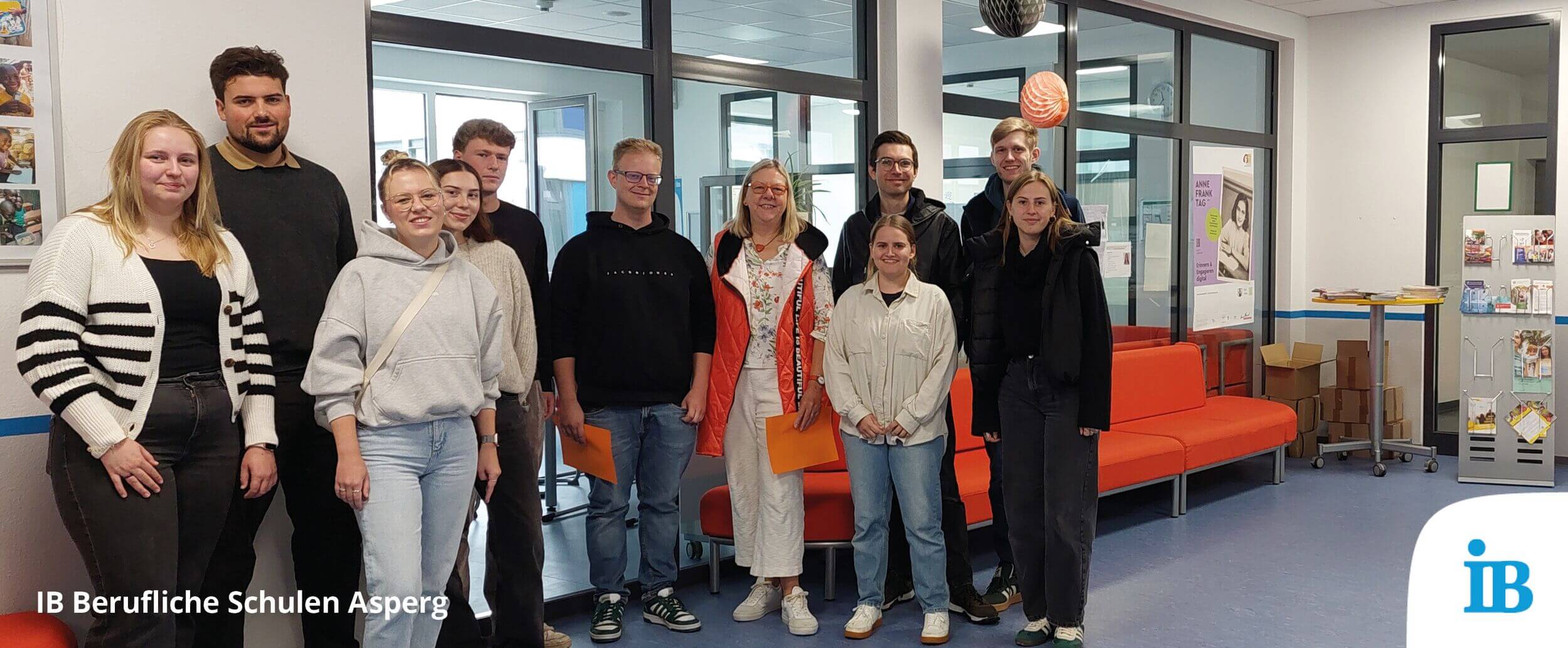 Eine Gruppe von Menschen steht zusammen lächelnd in einer modernen Lobby der IB Beruflichen Schulen Asperg.