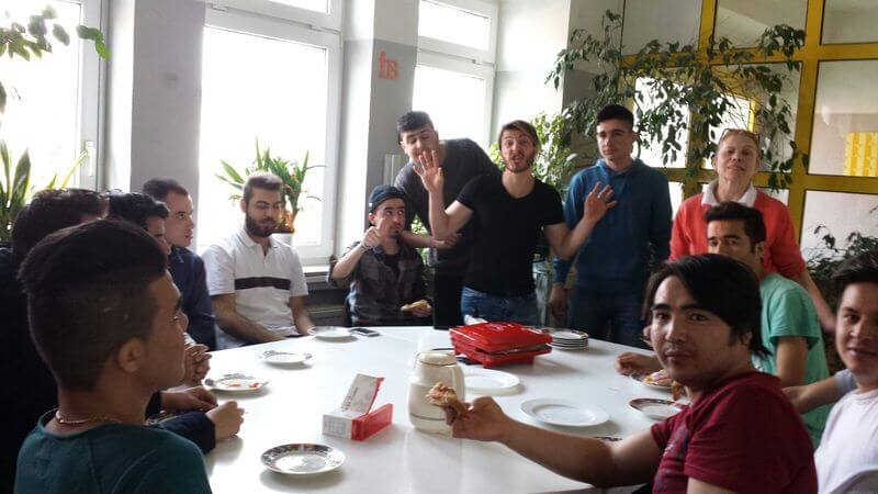 Eine Gruppe von Menschen sitzt um einen Tisch und genießt gemeinsam eine Mahlzeit in einem sonnigen Raum.