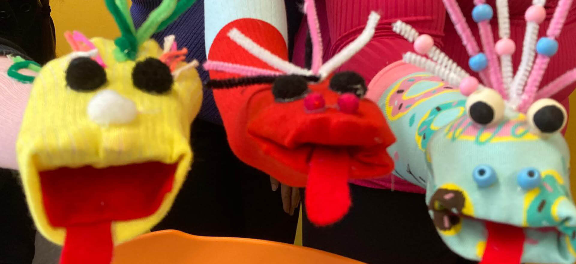 Bunte Handpuppen mit fröhlichen Gesichtern werden von drei Personen präsentiert.