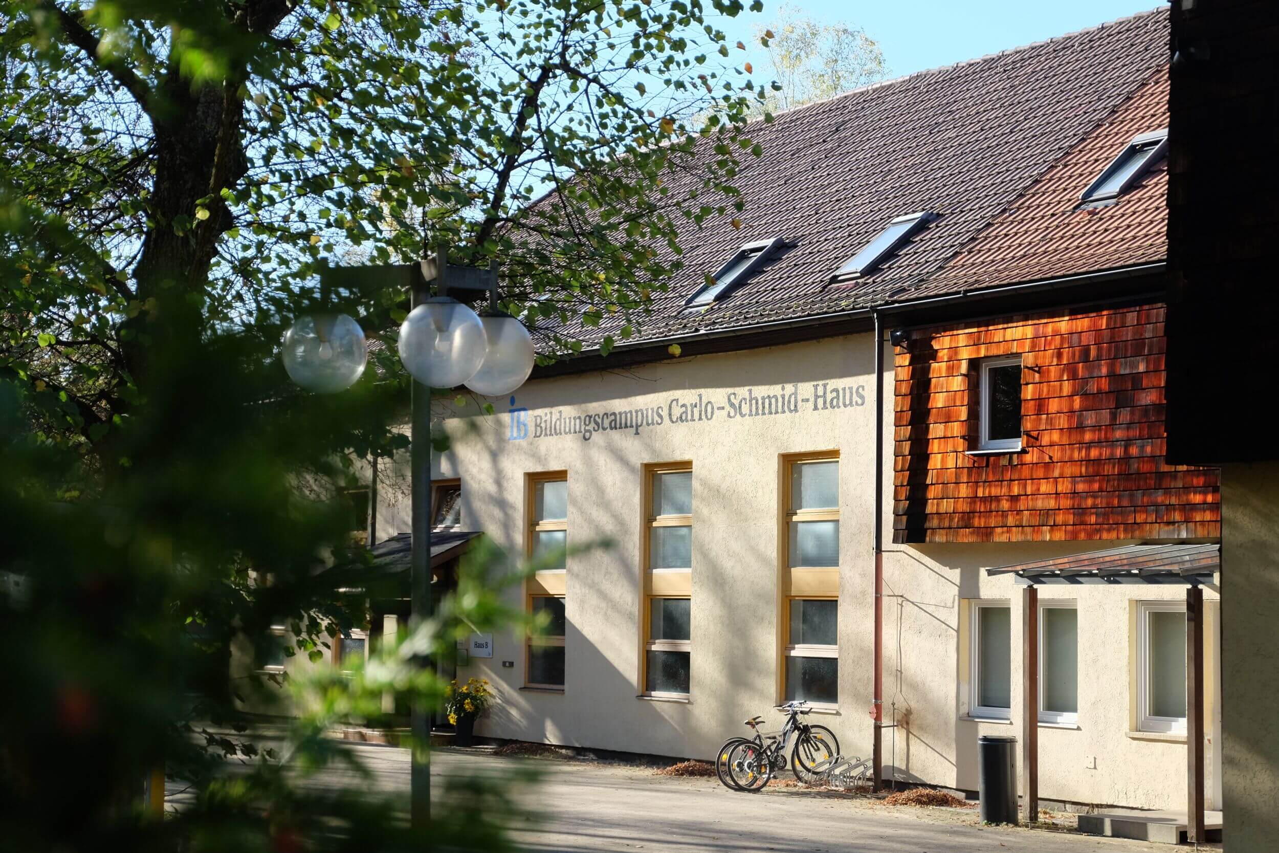 Das Bildungszentrum Carlo-Schmid-Haus steht unter blauem Himmel, umgeben von Bäumen, mit zwei Fahrrädern davor.