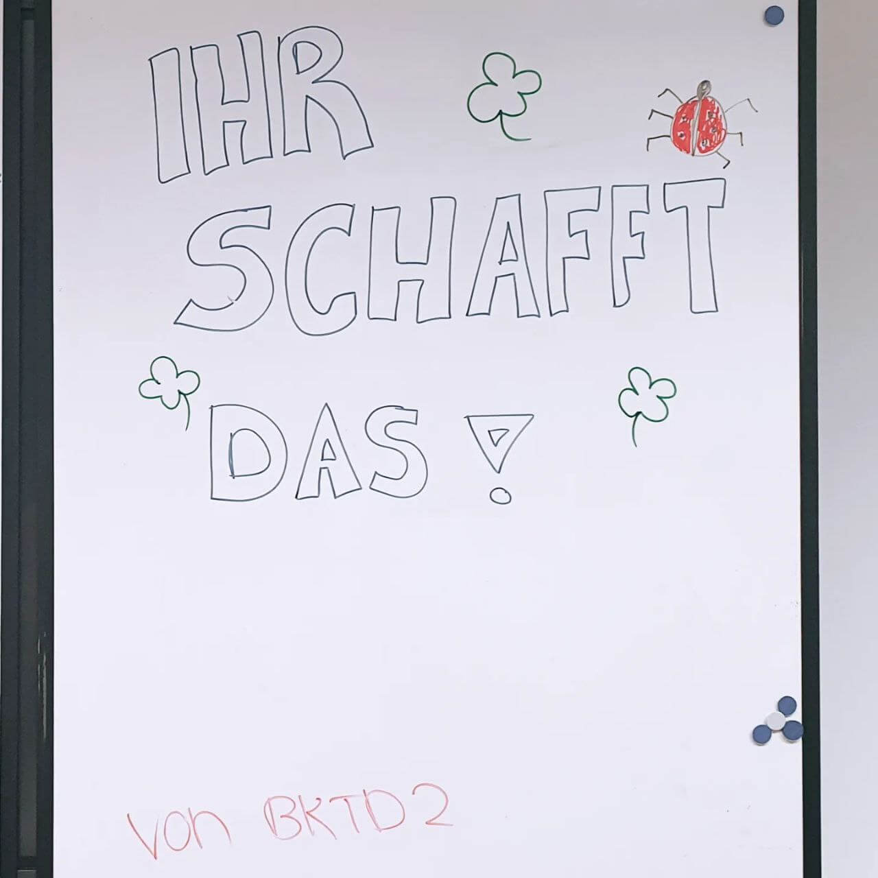 Eine Tafel zeigt die motivierende Botschaft "Ihr schafft das!" mit Klee und einem Marienkäfer verziert.