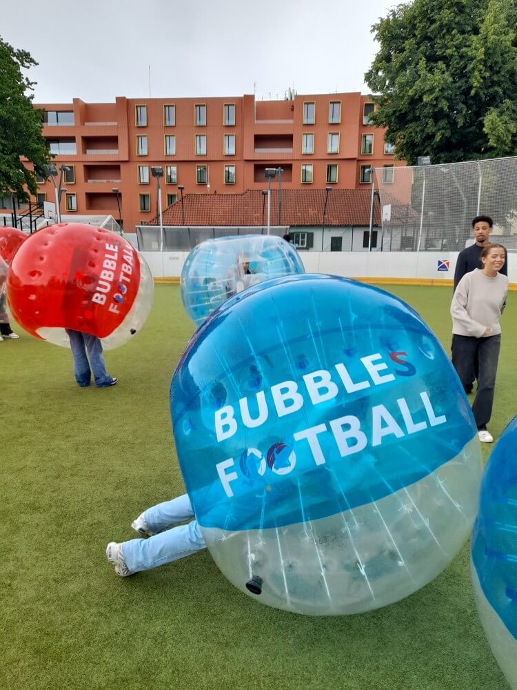Spieler in aufblasbaren Bällen auf dem Feld beim Bubble Football, umgeben von grüner Rasenfläche und Gebäuden.