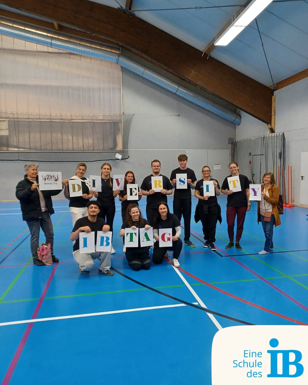 Eine Gruppe hält Plakate mit dem Wort "DIVERSITY" beim IB-Tag in einer Sporthalle. | © IB