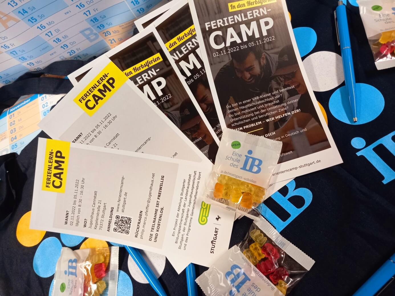 Flyer und Süßigkeiten für ein Ferienlern-Camp liegen auf einem Tisch neben einem Kalender und einem blauen Stift.