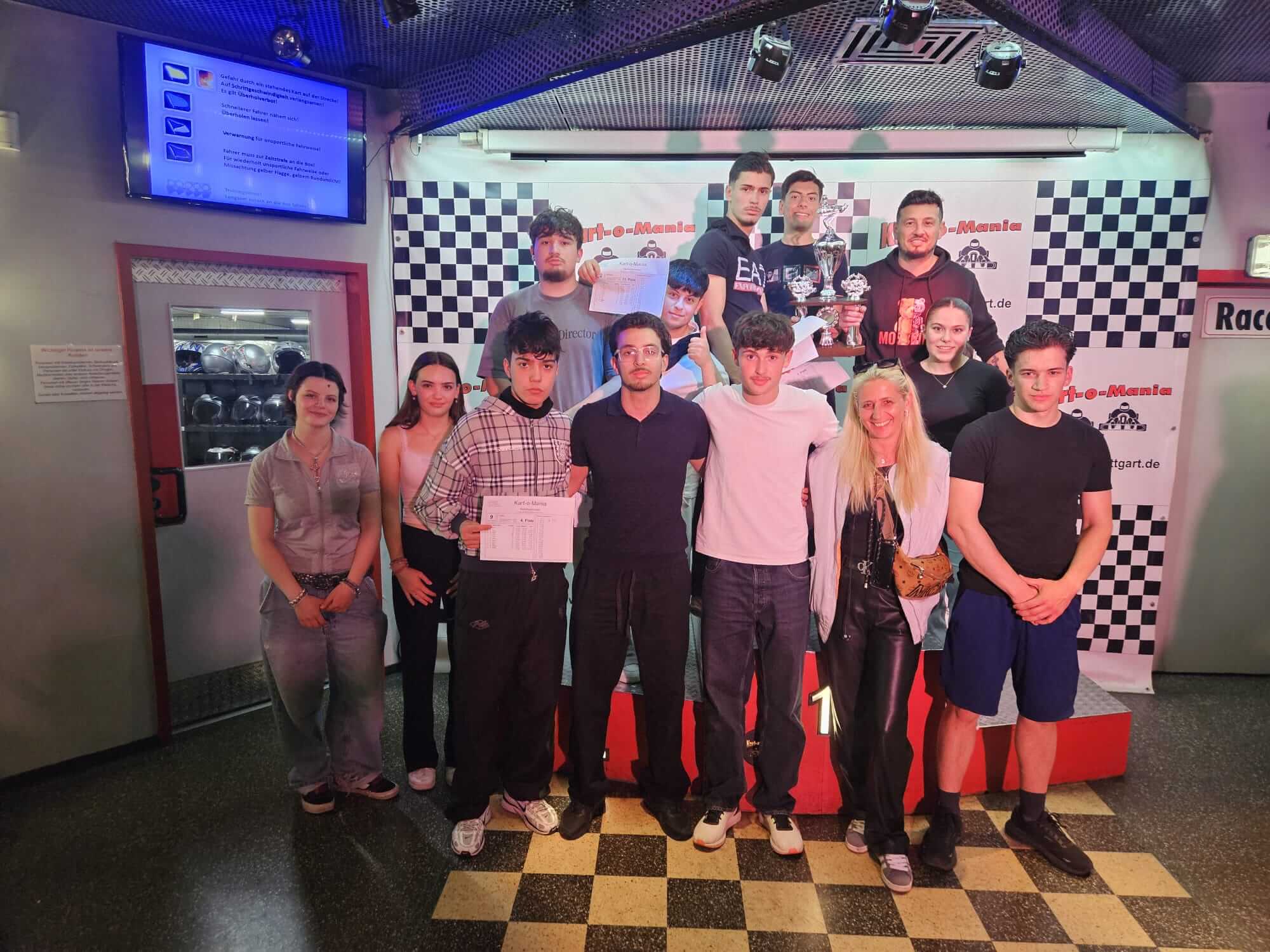 Gruppe von Menschen bei einer Preisverleihung in einer Kartbahn, lächelnd und stolz mit Trophäen in der Hand. | © Name