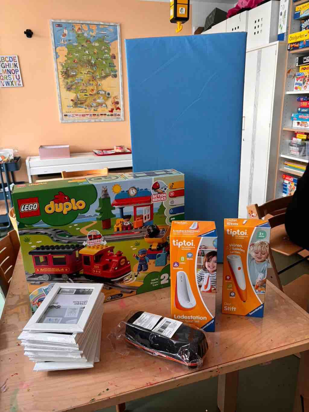 Auf einem Tisch liegen ein Lego Duplo Set, Tiptoi Produkte und weitere Schulmaterialien in einem Klassenzimmer.